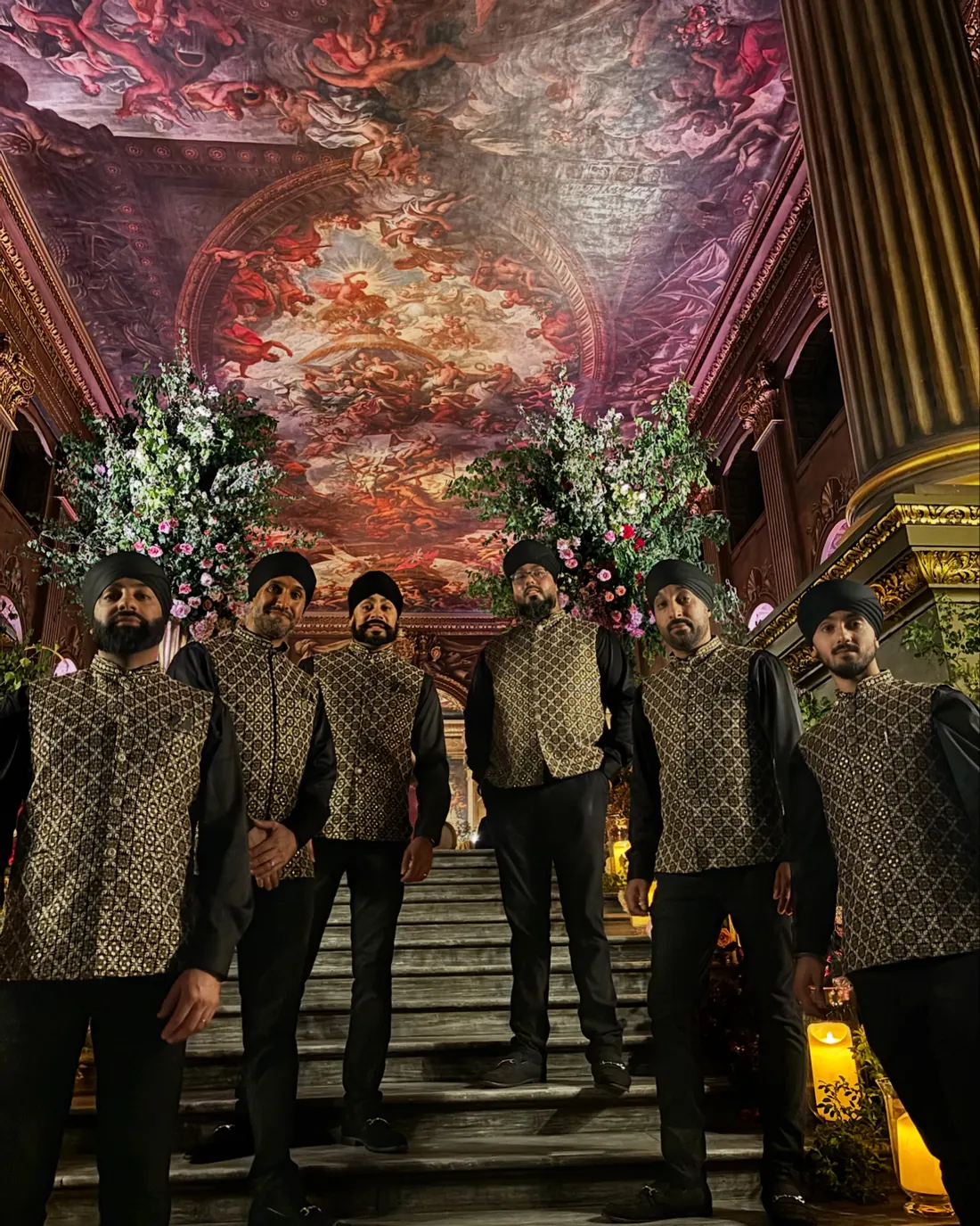 Dhol players in black outfits with gold embroidered waistcoats in a grand hall