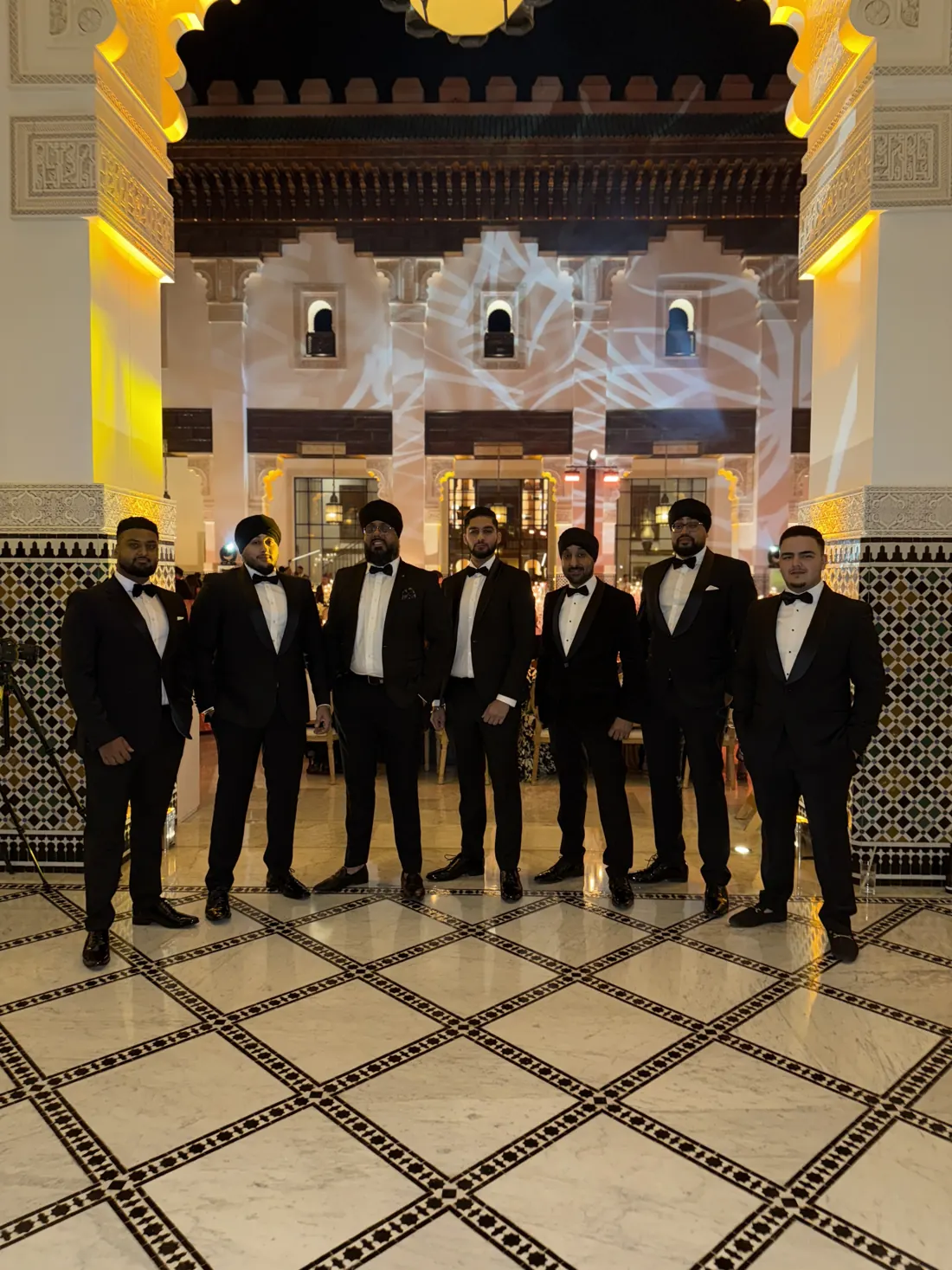 A team of dhol players in black tie standing in a hotel lobby
