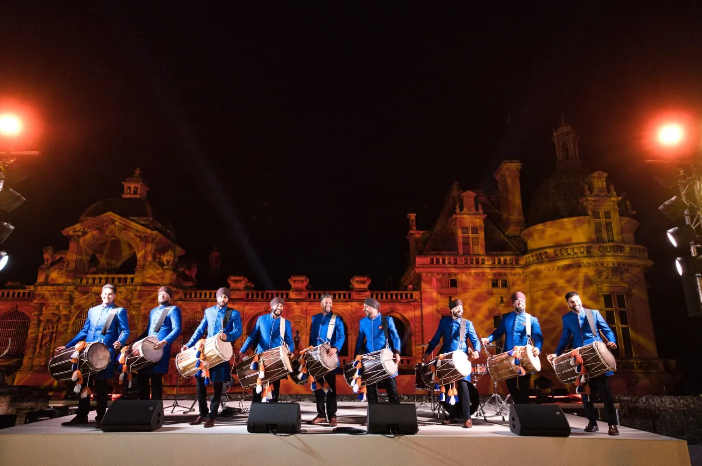 A team of dhol players in blue jackets performing on a stage in Paris